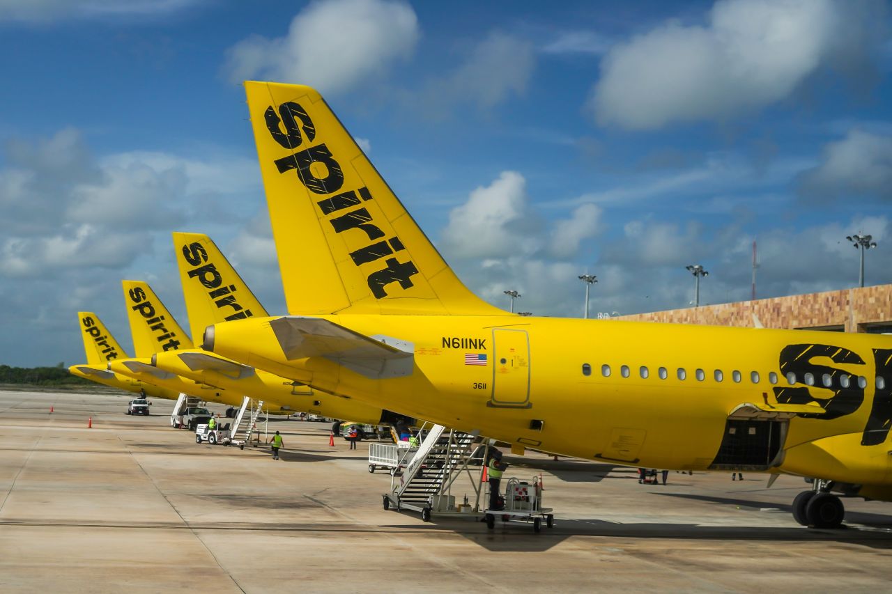 Spirit Airlines aircraft lined up on the tarmac under a blue sky, showing the carrier's signature yellow livery and bold black logo on the tail fins